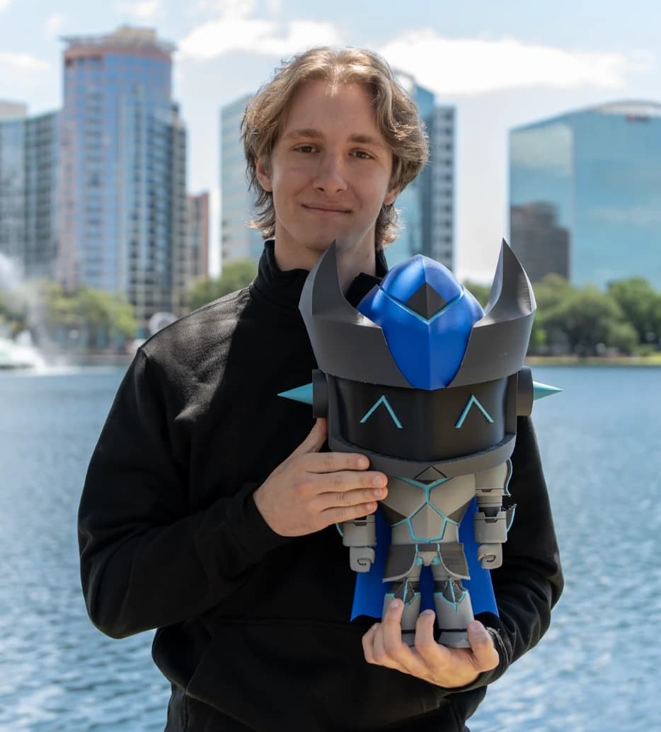 Michael Rusu holding a blue and black robot figure beside a lake.